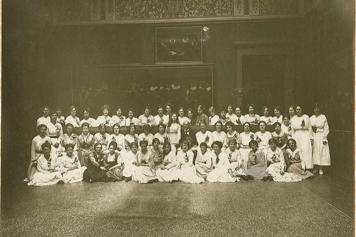 Foto van een groep van ruim 50 in het wit geklede dames met in hun midden een oudere man in jacquet.