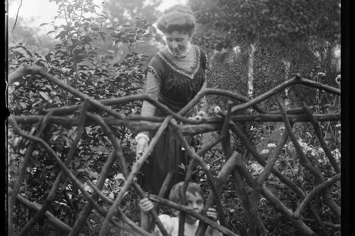 Glasnegatief van een foto van Delphine Cuypers-Povel met Charles Cuypers in de tuin achter een houten hekwerk