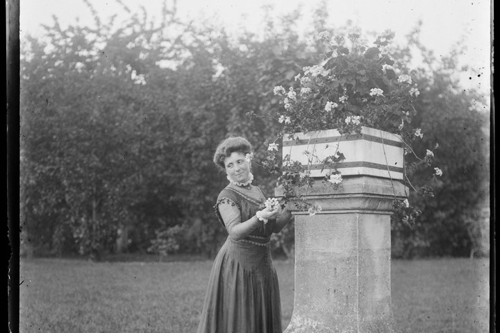 Glasnegatief van een foto van vrouw in tuin bij bloemenzuil